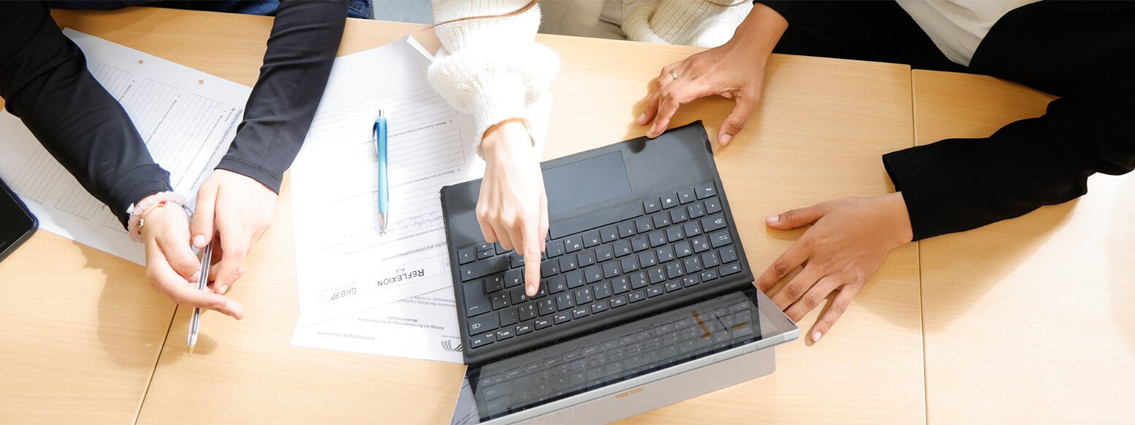 An einem Laptop arbeiten ein paar Schülier/-innen, die man im Anschnitt sieht