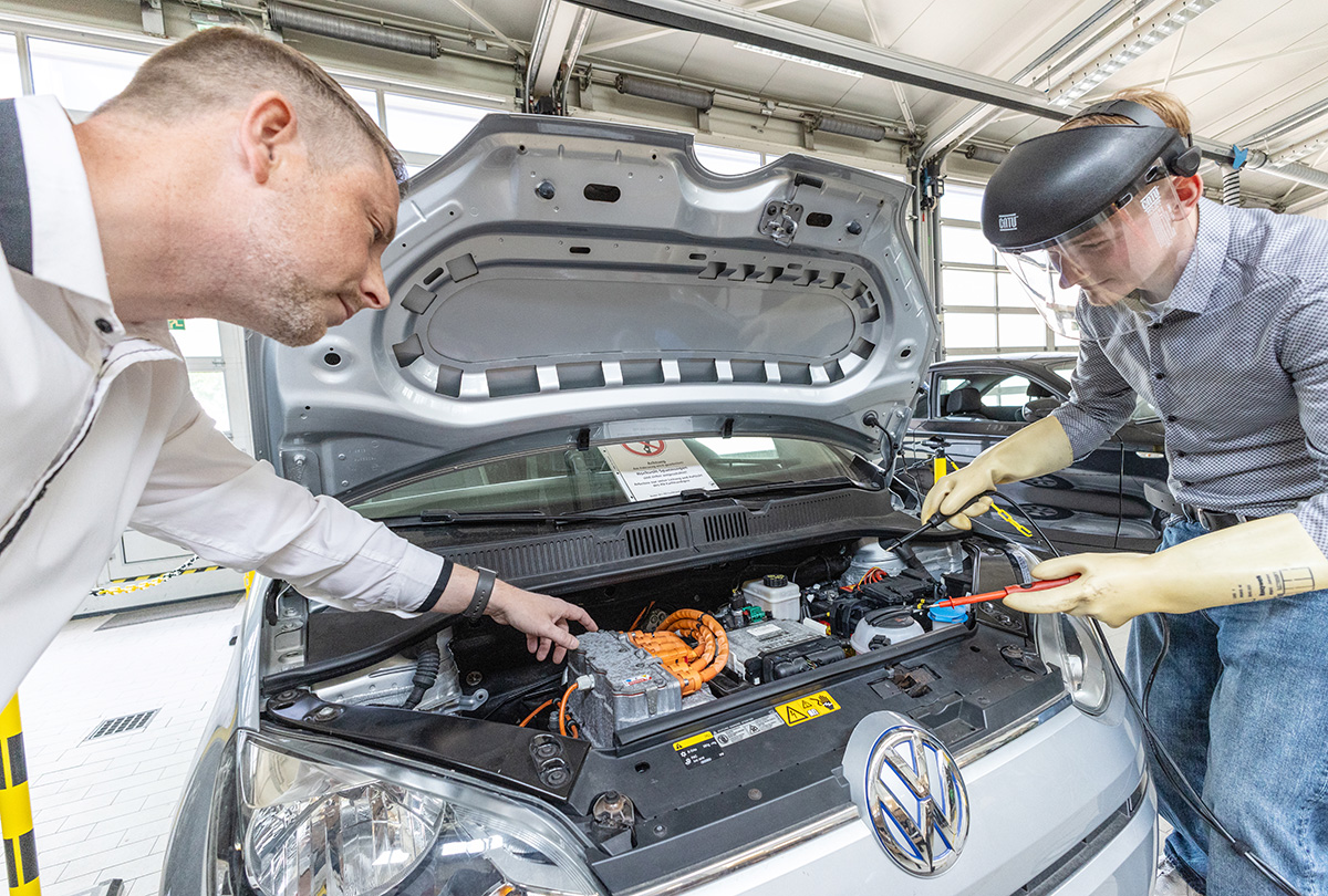 Schüler und Lehrer arbeiten an einem geöffneter KFZ-Motorhaube