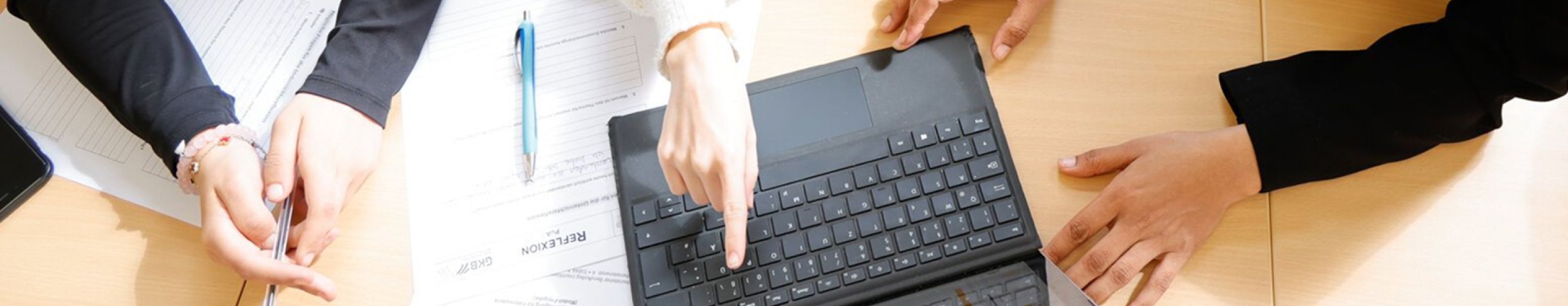 An einem Laptop arbeiten ein paar Schülier/-innen, die man im Anschnitt sieht